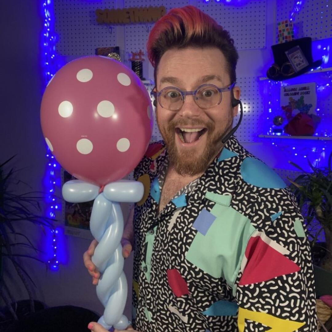 Dave Brenn holding a pink polka dot balloon sculpture with a big smile during a balloon entertainment show.